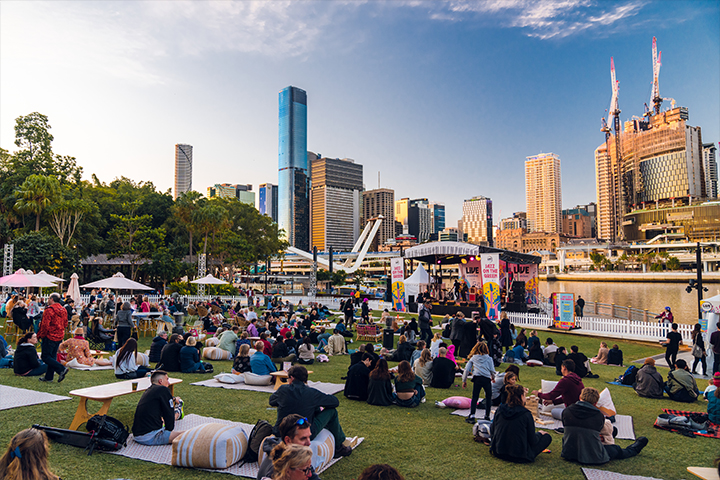 A group of people sitting on the grass watching an outdoor movie by the Brisbane River.